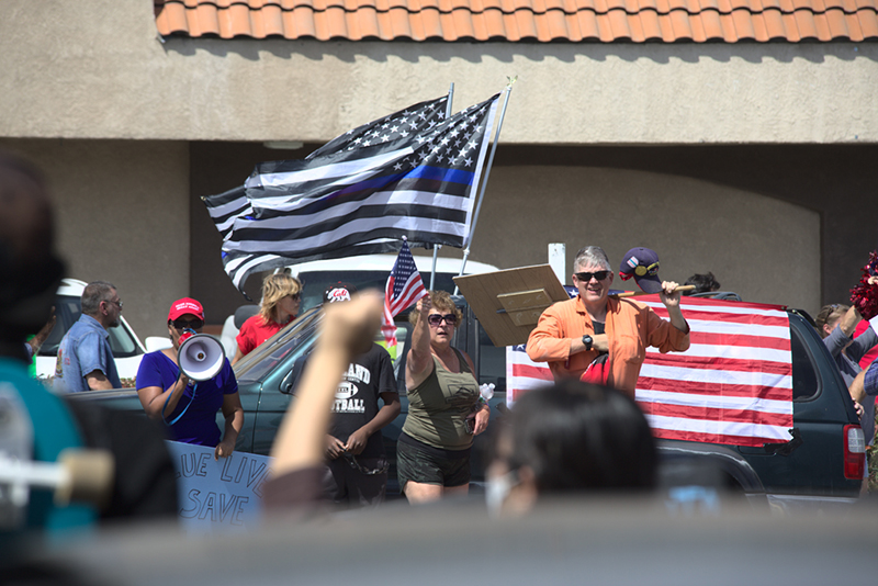 Group of people, one with a megaphone, others waving an American flag and altered American (blue line) flags.