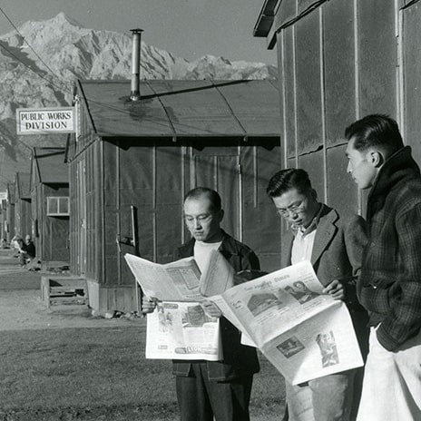 Men reading newspaper at Manzanar