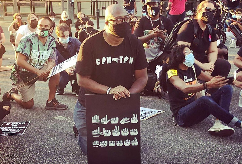 People kneeling in a street while holding signs of protest.