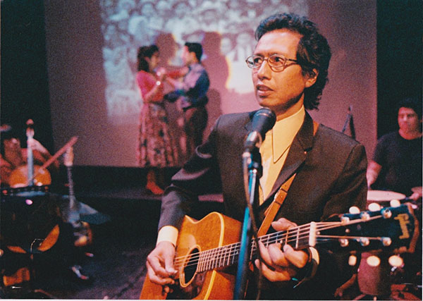 Man playing guitar while a coupe dances in the background