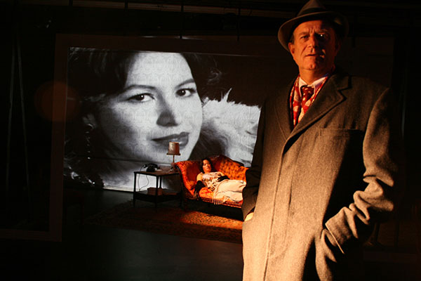 Man standing while a woman reclines on a couch in the background