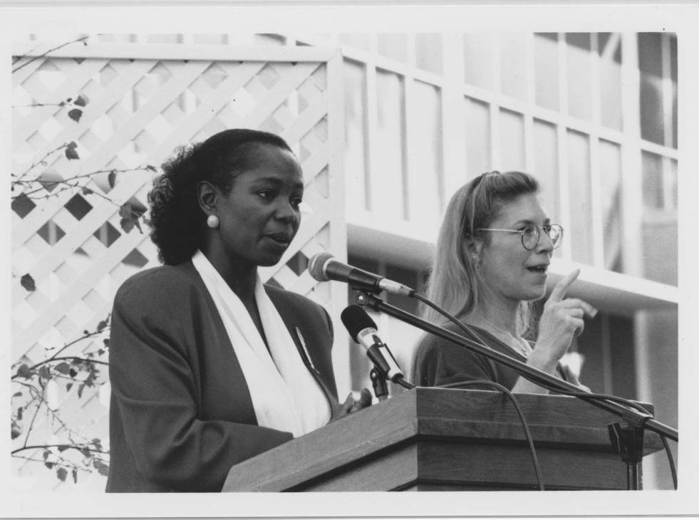 A woman standing in front of a microphone and another woman standing next to her.