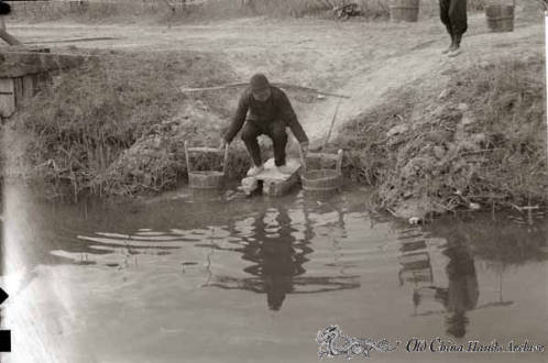 Man filling buckets with water from the nearby river in the countryside near Tientsin, spring 1946