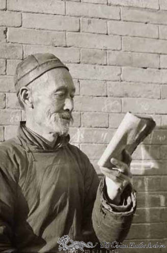 Elderly Chinese man reads a book in front of a wall on a Tientsin street in 1946