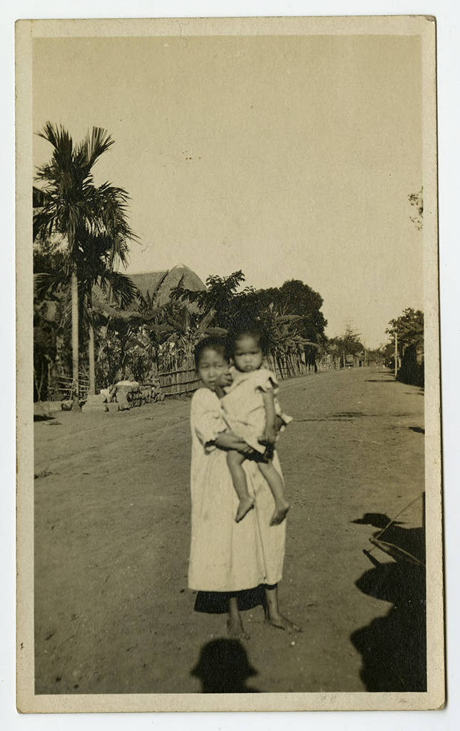 Young girl holding a child in a village, ca. 1910