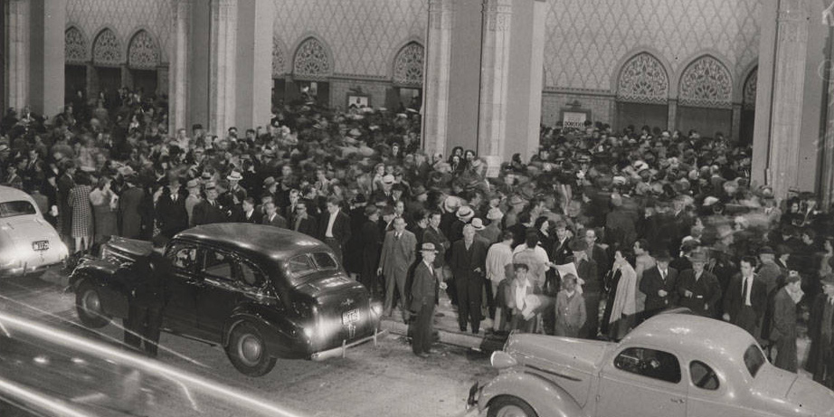 Cars driving by a gathered crowd