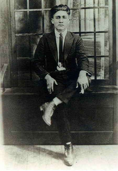 Photo of Antonio Calvo, circa 1920s, wearing a suit and sitting on a bench with legs crossed.