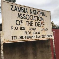 Sign reading Zambia National Association of the Deaf, P. I. Box 35821 Lusaka PLOT 10437. Tel: 260-01-286247 FAX: 260-1-286248