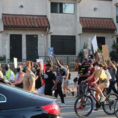 Masked marchers, some on bicylces, carrying signs