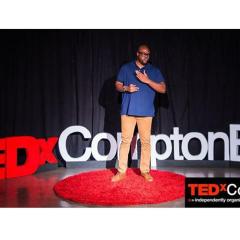 man on a stage in front of a sign that reads TEDx Compton Blvd