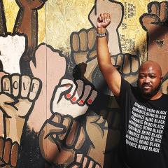 man raises a clenched fist in front of a mural of clenched fists