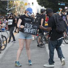 Masked woman holding handmade sign in the middle of a march:  FUCK the SHERIFF!