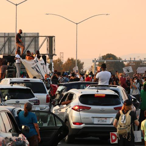 Cars and protesters clustered on the freeway, some people standing on cars