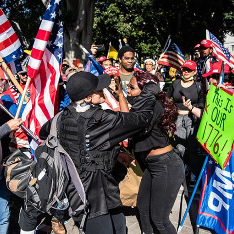 People with Trump campaign and American Flags attack a black woman; on carries a sign: This Is OUR 1776!