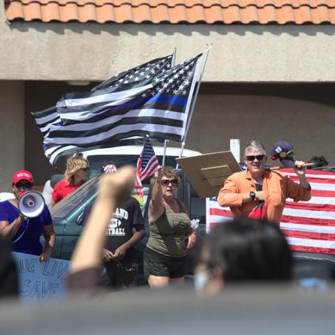 Group of people, one with a megaphone, others waving an American flag and altered American (blue line) flags.