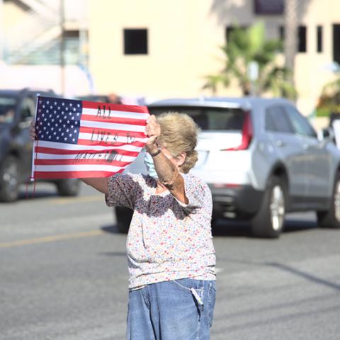 Woman waves American flag with the message "All Lives Matter"