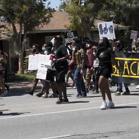 Woman marching with a megaphone in front of the West Valley Black Lives Matter banner