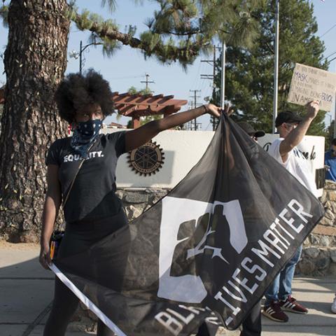 Woman with face scarf waves large BLACK LIVES MATTER flag.