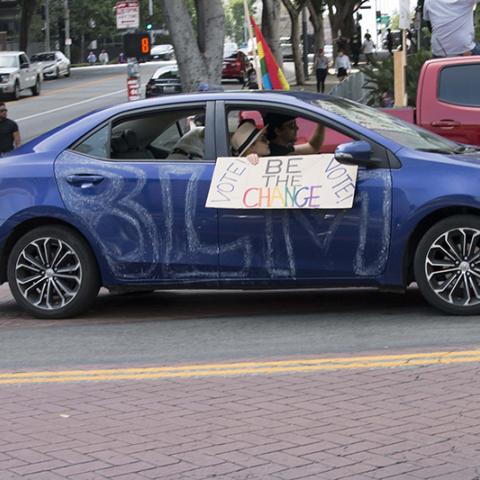 Car painted with BLM, passenger holding sign out the window:  VOTE! BE THE CHANGE - VOTE!