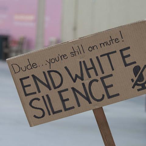Cardboard sign: Dude…you're still on mute!  END WHITE SILENCE