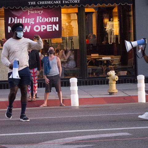 In the street, a woman speaks through a megaphone while a man holding a megaphone stands nearby