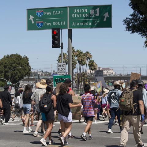 Large crowd of people marching with signs near a freeway onramp