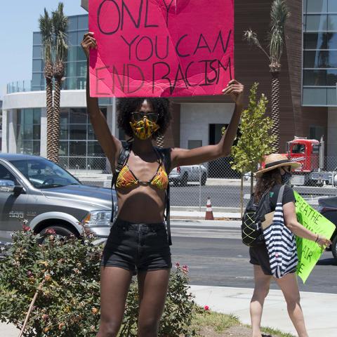 Masked woman holds a handmade sign: ONLY YOU CAN END RACISM