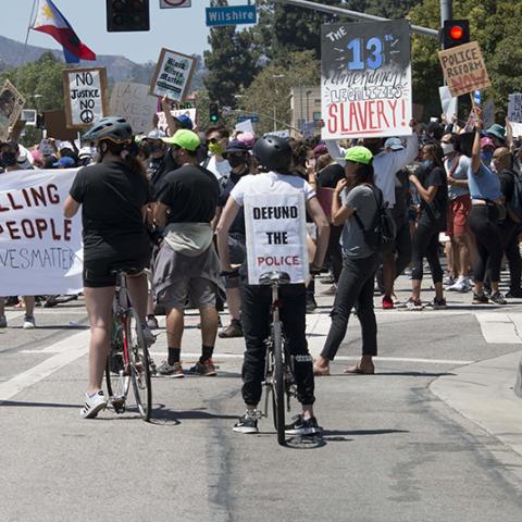 Large crowd of people in a street intersection with signs and banners that include: STOP KILLING BLACK PEOPLE; DEFUND THE POLICE; THE 13th Amendment LEGALIZES SLAVERY!; POLICE REFORM NOW; FUCK TRUMP; BLACK LIVES MATTER