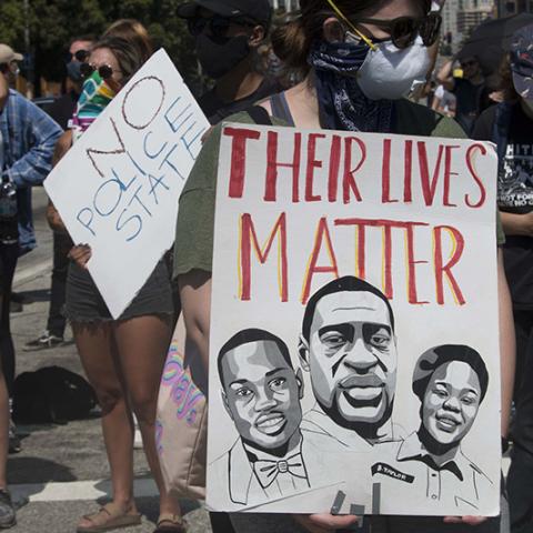 Two signs: NO POLICE STATE; THEIR LIVES MATTER (with drawings of two men and one woman)