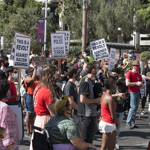 Large crowd of masked people in a street with signs that include: JUSTICE FOR JACOB BLAKE; THIS IS A REVOLT AGAINST RACISM; END RACIST POLICE AND VIGILANTE TERROR 