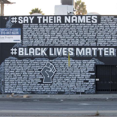 Side of a two-story building covered with a mural: JUSTICE 4, #SAY THER NAMES, #BLACK LIVES MATTER and many names.