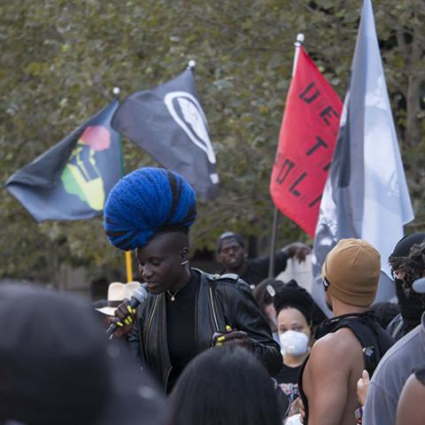 Speaker speaking through microphone, with 5 flags in the background