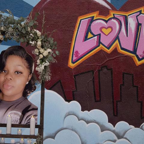 Shrine decorated with candles and flowers and a photo of Breonna Taylor, mural of Love in the background