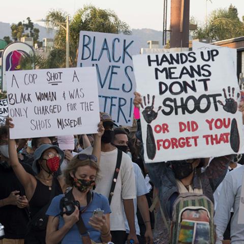 Masked marchers with signs: DEFUND THE POLICE; JUSTICE FOR BREONNA; A COP SHOT A BLACK WOMAN & WAS ONLY CHARGED FOR THE SHOTS MISSED!!!; BLACK LIVES MATTER!; HANDS UP MEANS DON'T SHOOT OR DID YOU FORGET THAT