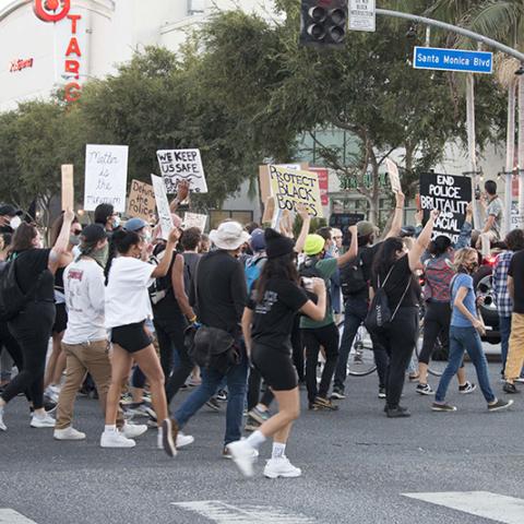 Large crowd of masked people in a street with signs that include: BLACK LIVES MATTER; Matter is the Minimum; Defund the Police; WE KEEP US SAFE; PROTECT BLACK BODIES; END POLICE BRUTALITY