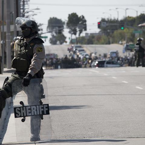 Officer from the Sheriff's department stands with a shield by the curb