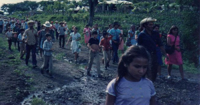 People walking along a dirt road surrounded by trees.