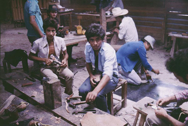 Men looking at camera while working on shoes.