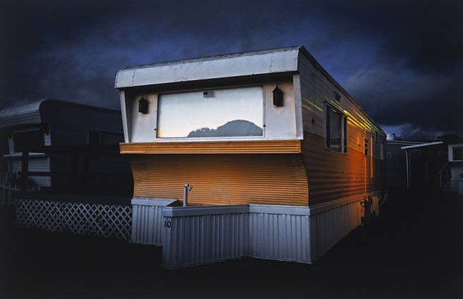 Trailer in brown and white mounted on white wooden foundation under cloudy night sky.