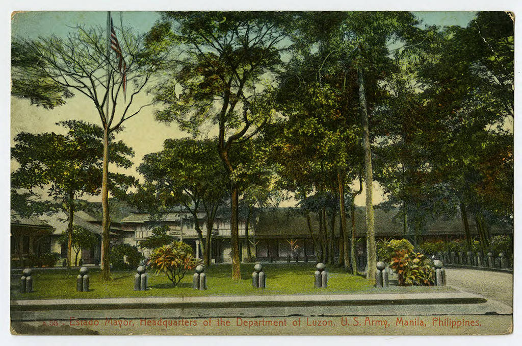 Colorized photograph of a building with tall trees, hedges, a lawn with decorative boundry markers, and an American flag.